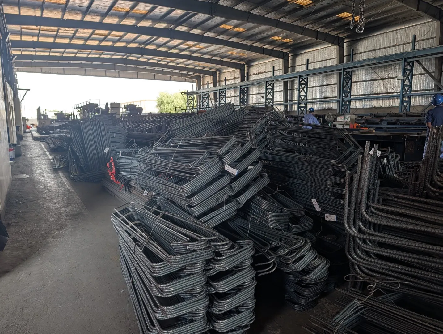 Factory floor at Dubar in Dubai Investments Park, with bundles of cut and bent reinforcement bars and staff in safety helmets at the machines